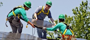 建築作業員と一緒に太陽光パネルを設置するマイケル・ベネット米上院議員 （中央）(© AP Images)