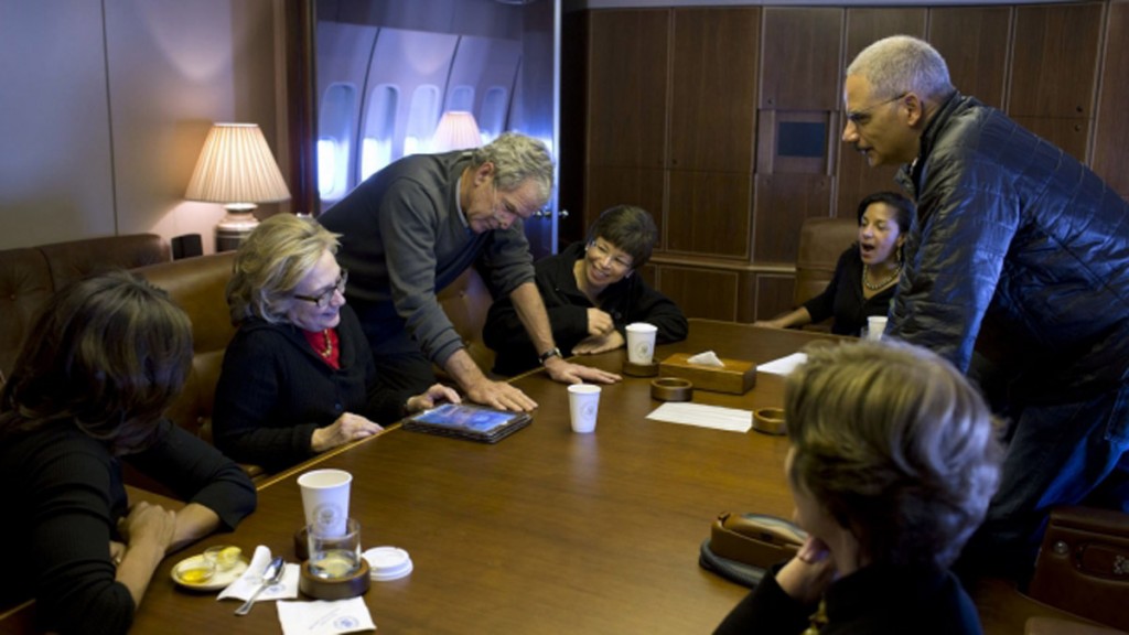 Aboard Air Force One, former President George W. Bush shows photos of his paintings to first lady Michelle Obama, former Secretary of State Hillary Rodham Clinton, Obama staff and Cabinet members, and Laura Bush. (White House)