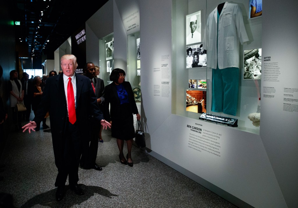 住宅都市開発長官に指名したベン・カーソン博士に関する展示コーナーを訪れたトランプ大統領。カーソン夫妻が同行した  (© AP Images)
