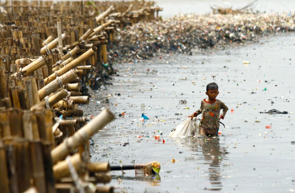 インドネシア・ジャカルタの漁村で廃棄物からお金に換えられる物を集める子ども (© Solo Imaji/Barcroft Media via Getty Images)