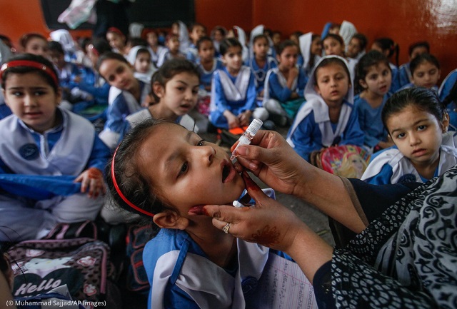 A health worker gives a polio vaccination to a student in Peshawar, Pakistan, in April 2019. (© Muhammad Sajjad/AP Images)