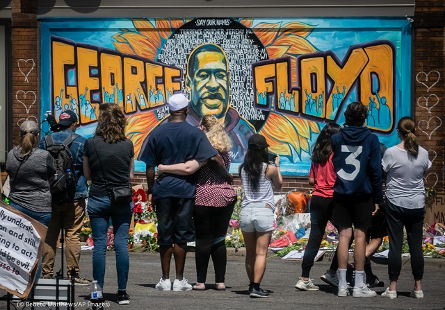 ミネアポリスの殺人現場に作られた壁画と追悼所を訪れジョージ・フロイドさんに黙とうを捧げる人々 (© Bebeto Matthews/AP Images)