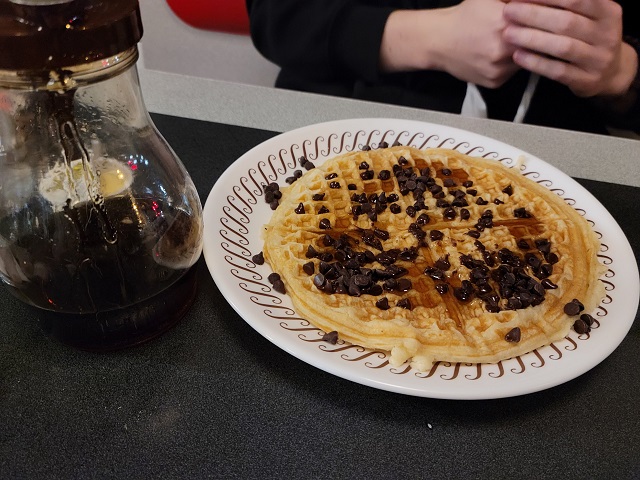 A chocolate chip waffle covered in syrup.