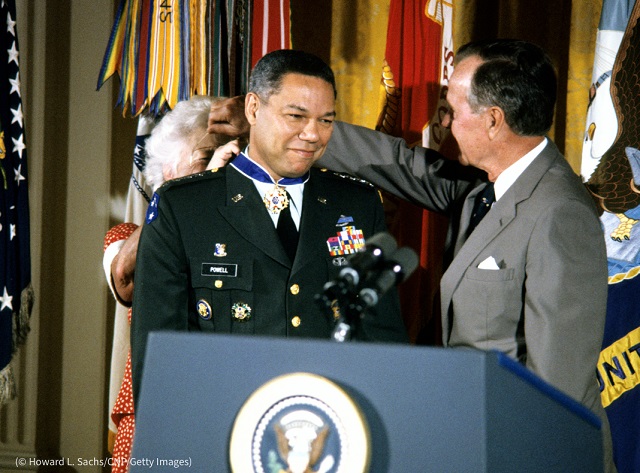 ホワイトハウスで開かれた授賞式で、ジョージ・H・W・ブッシュ大統領が見守る中、バーバラ・ブッシュ大統領夫人に大統領自由勲章のメダルをつけてもらうパウエル。1991年7月3日、首都ワシントンにて (© Howard L. Sachs/CNP/Getty Images)
