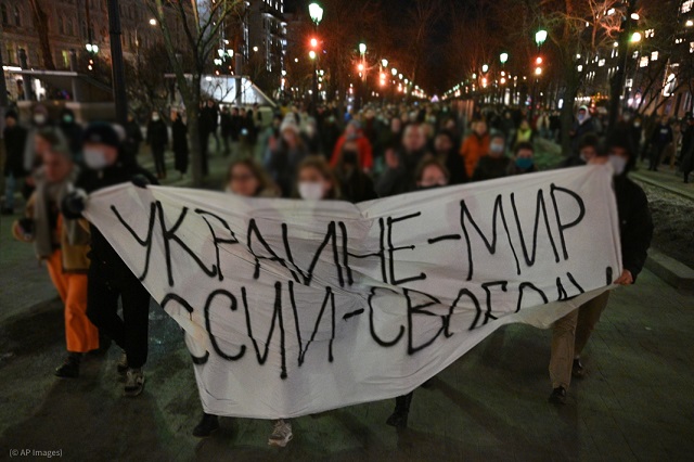 2月24日、モスクワで「ウクライナ―平和、ロシア―自由」と書かれた横断幕を持ってデモ行進する参加者。身元が特定されないよう顔にはぼかしを入れている (© AP Images)