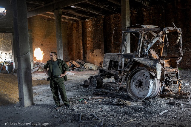 チェルカシーロゾバヤ。5月のロシアによる爆撃で破壊されたトラクターの横に立つ農家の男性。男性によると、ロシアは穀物倉庫と農業機材も破壊し、ハルキウ郊外の領土を支配している (© John Moore/Getty Images)