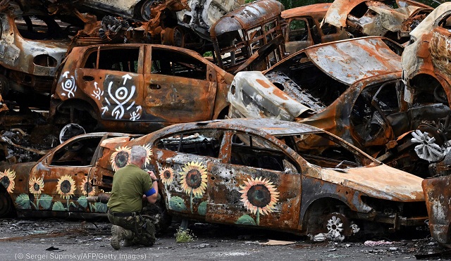 A Ukrainian service member crosses himself at the symbolic cemetery of cars shot by Russian troops, some painted by local artists, in Irpin, Ukraine, August 9. (© Sergei Supinsky/AFP/Getty Images)