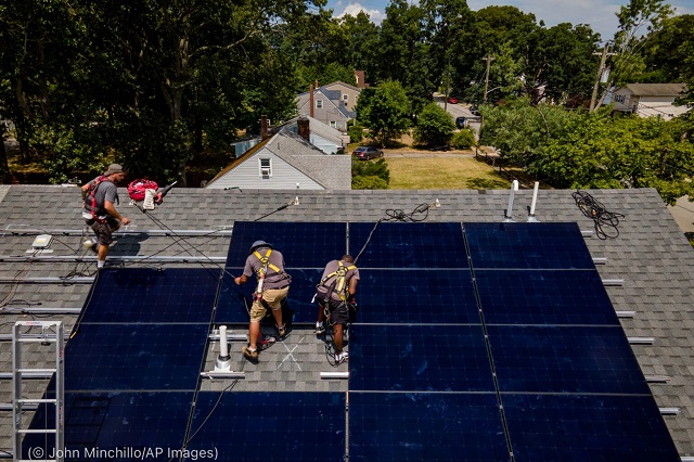 太陽光パネルを設置するニューヨーク・ステート・ソーラー社の社員。 8月11日、ニューヨーク州マサペクアにて(© John Minchillo/AP Images)