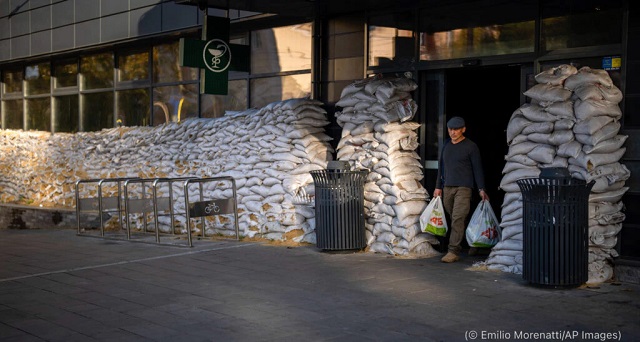A man carrying shopping bags leaves a supermarket protected by sandbags in the center of Mykolaiv, Ukraine, on October 24. (© Emilio Morenatti/AP Images)