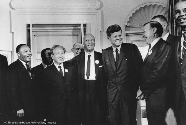 1963年8月28日、ホワイトハウスで「仕事と自由のためのワシントン大行進」のリーダーたちに笑顔を見せるジョン・F・ケネディ大統領。左から、キング牧師、ジョン・ルイス、ヨアヒム・プリンツ、ユージン・カーソン・ブレイク、A・フィリップ・ランドルフ、ケネディ、ウォルター・ロイター、ロイ・ウィルキンス。ロイターの背後はリンドン・ジョンソン副大統領 (© Three Lions/Hulton Archive/Getty Images)